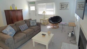 Un salon avec un canapé marron, une table basse blanche, un fauteuil en osier et un téléviseur.