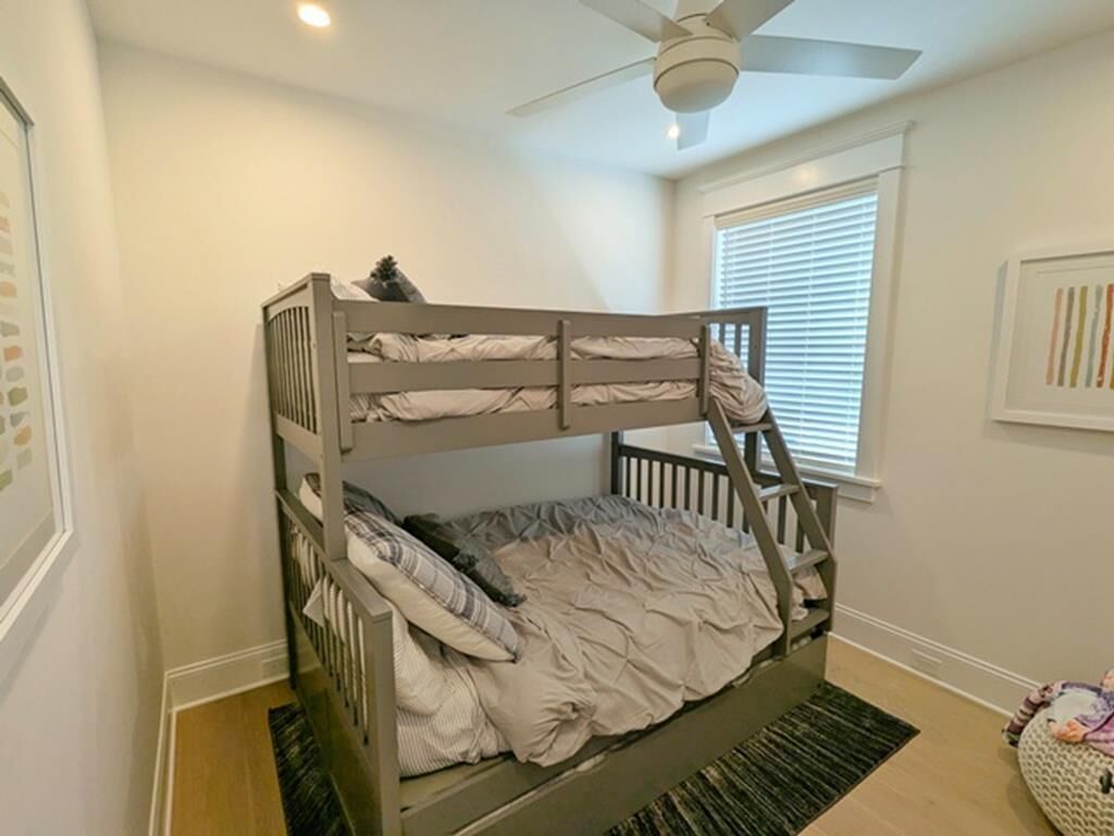 Ein Stockbett in einem Zimmer mit Deckenventilator, Jalousiewindfang und einem gerahmten Bild an der Wand.