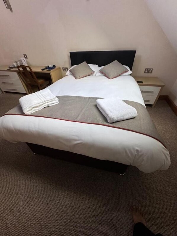 A neatly made bed with white and grey bedding, a wooden headboard, and a small bedside table with a lamp. - The Clubhouse (Sheffield)