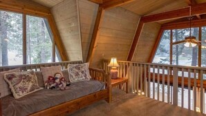 A cozy attic bedroom with a wooden bunk bed, a small table with a lamp, and a view of the snowy forest outside. -  Inviting Central Oregon Escape (Sunriver)