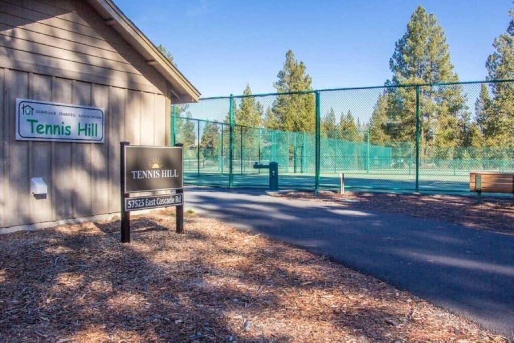 A tennis court with a fence, a bench, and a sign indicating 'Tennis Hill' and '57525 East Cascade Rd.'