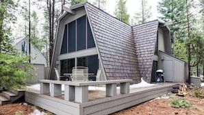 A modern cabin with a sloped roof, large windows, and a deck with outdoor furniture. -  Inviting Central Oregon Escape (Sunriver)