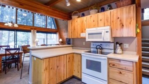 A kitchen with wooden cabinets, a microwave, a stove, and a dining area with chairs and a table. -  Inviting Central Oregon Escape (Sunriver)