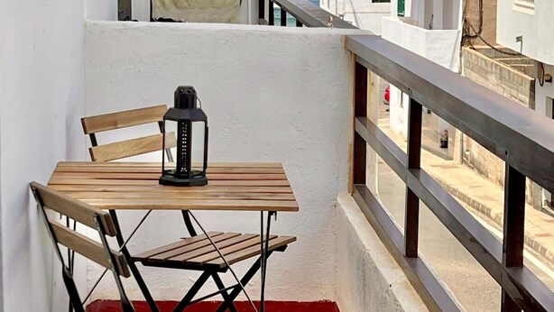 Un balcone con tavolo e sedie in legno, una lanterna e vista sul mare e sugli edifici bianchi.
