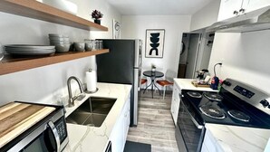 A compact kitchen with a microwave, stove, and shelves with dishes. - Jr. Suite ATLAS- The Agustin Guesthouse for Men, a beautiful & sexy resort oasis (Fort Lauderdale)