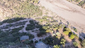 An aerial view of a coastal area with a dirt road, sparse vegetation, and a small building with a solar panel. - Unique villa 400 m from secluded beach with panoramic views, reached by 4x4 (Baja California Sur)