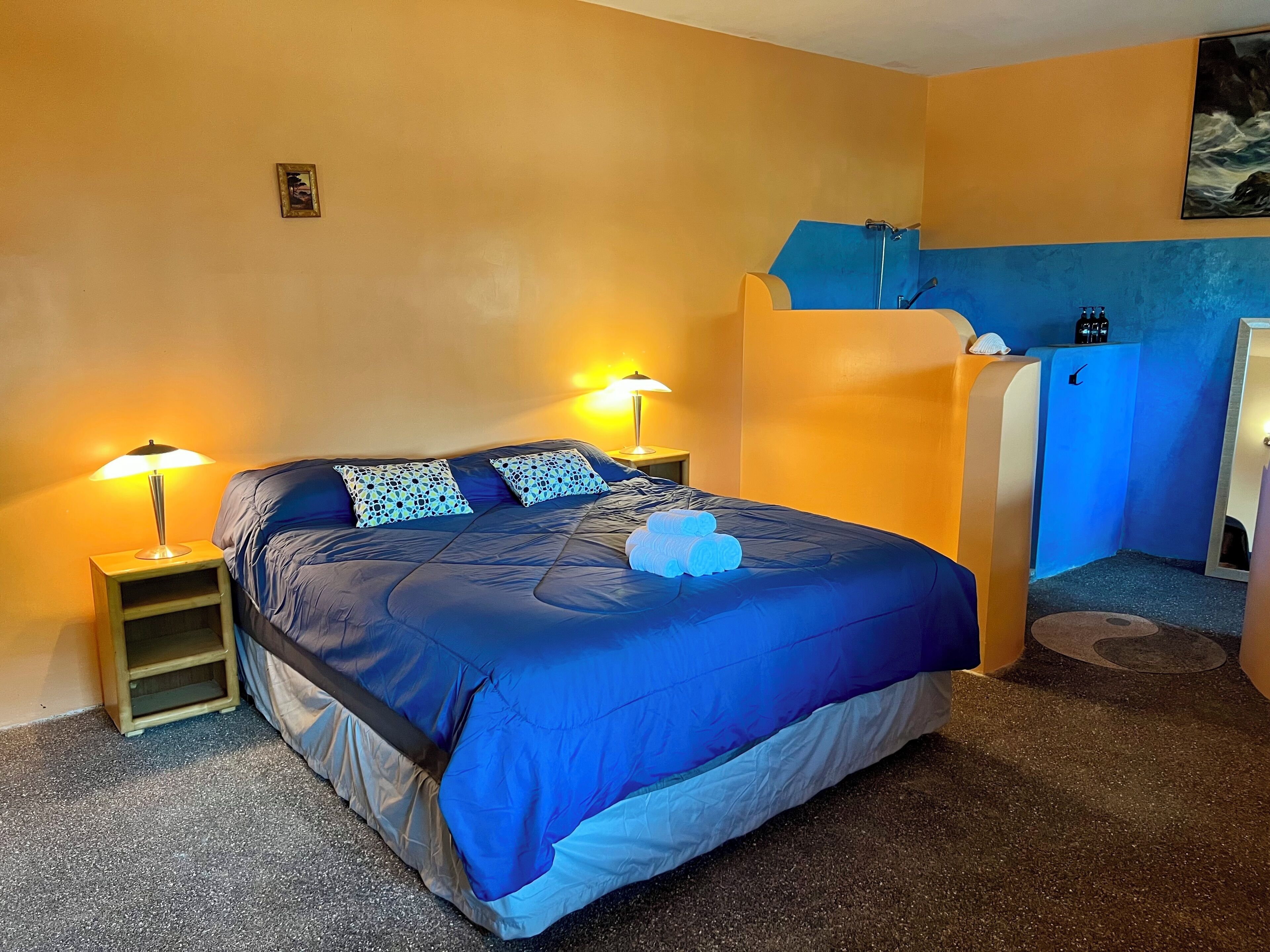 Ein Schlafzimmer mit einem Bett, zwei Nachttischlampen, einer blauen Wand, einem kleinen Regal und einem blauen, an der Wand befestigten Regal.