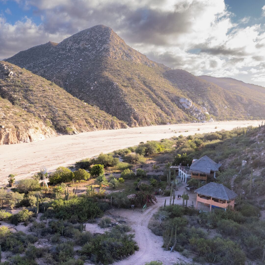 A desert landscape with a mountain, a beach, and a small building with a thatched roof.