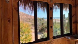 A wooden cabin with large windows overlooking a desert landscape with cacti and a beach. - Unique villa 400 m from secluded beach with panoramic views, reached by 4x4 (Baja California Sur)