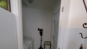 Een smalle gang met betegelde vloer, een staande lamp en een prullenbak.