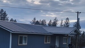 Een gelijkvloers huis met een blauwe buitenkant, een overdekte veranda met een tafel en stoelen, en een kleine voortuin.