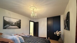 Une chambre à coucher avec un grand lit, un lustre, une porte et un tableau encadré au mur.