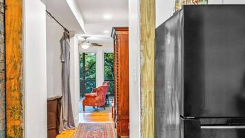Un couloir avec un réfrigérateur noir, une chaise rouge et un tapis à motifs.