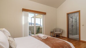 Ein Schlafzimmer mit einem Bett, einem Sessel, einer Schiebetür zum Balkon und einem Duschbereich.
