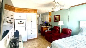 A compact room with a bed, a desk, a chair, a fan, and a kitchenette. - 5 O'Clock Somewhere (North Myrtle Beach)