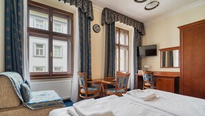 Habitación de hotel con dos camas, un escritorio, una silla, un televisor y una ventana con cortinas.