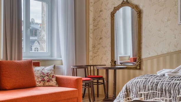 Hotellihuoneessa on sohva, pieni pöytä ja tuoli, sänky sekä suuri peili seinällä.