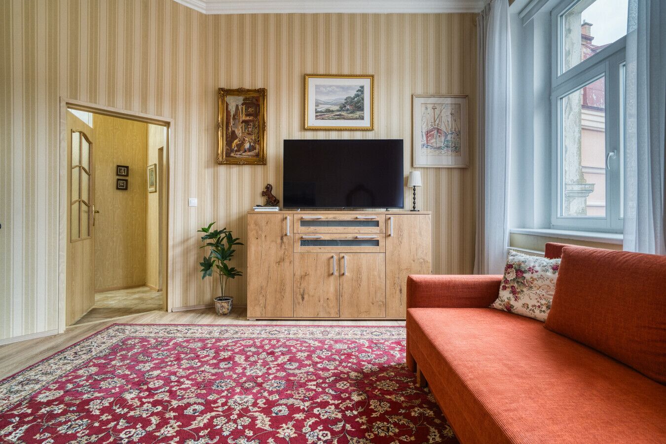 Un salon avec un meuble en bois, un téléviseur, un canapé rouge et un tapis à motifs.