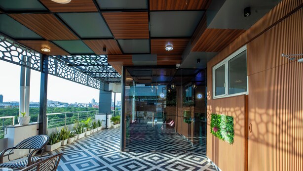 A modern outdoor terrace with geometric patterned flooring, wooden ceiling panels, and a view of the cityscape. - Aarchh Regency (Noida)