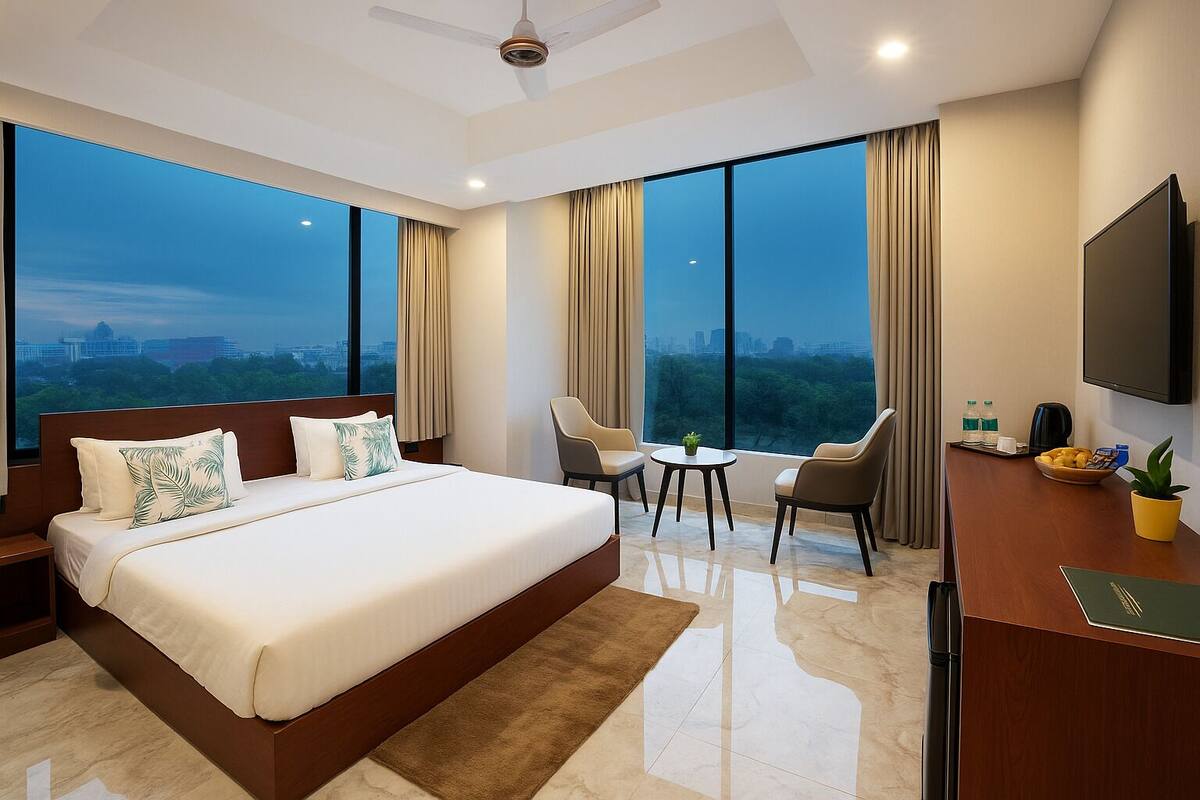 A modern hotel room with a large bed, a desk, two chairs, a TV, and a city view.
