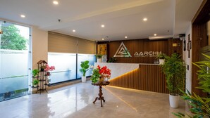 A reception area with a wooden reception desk, potted plants, and a marble counter. - Aarchh Regency (Noida)