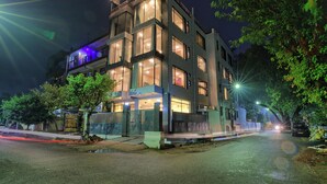 A multi-story building with illuminated windows and balconies, surrounded by trees and a street. - Aarchh Regency (Noida)
