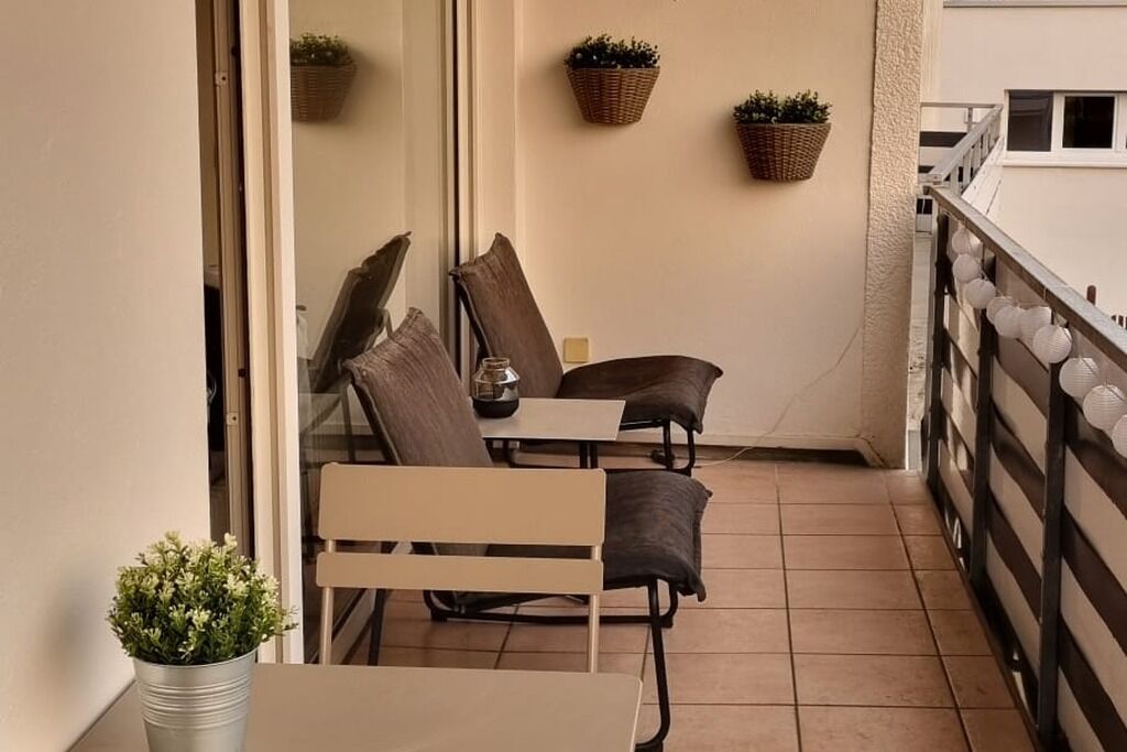 Ein kleiner Balkon mit zwei Stühlen, einem Tisch, Topfpflanzen und einem Geländer.
