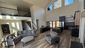 A spacious living area with a large sofa, a coffee table, and a dining table. There is a kitchen area with modern appliances and a staircase leading to an upper level. - RY Place: Relax. Refresh. Repeat. (Mountain Home)