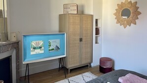 A room with a framed artwork on a stand, a wooden wardrobe, a mirror with a sunburst frame, and a hanging light fixture. - Maison Le Beaulieu (Vichy)