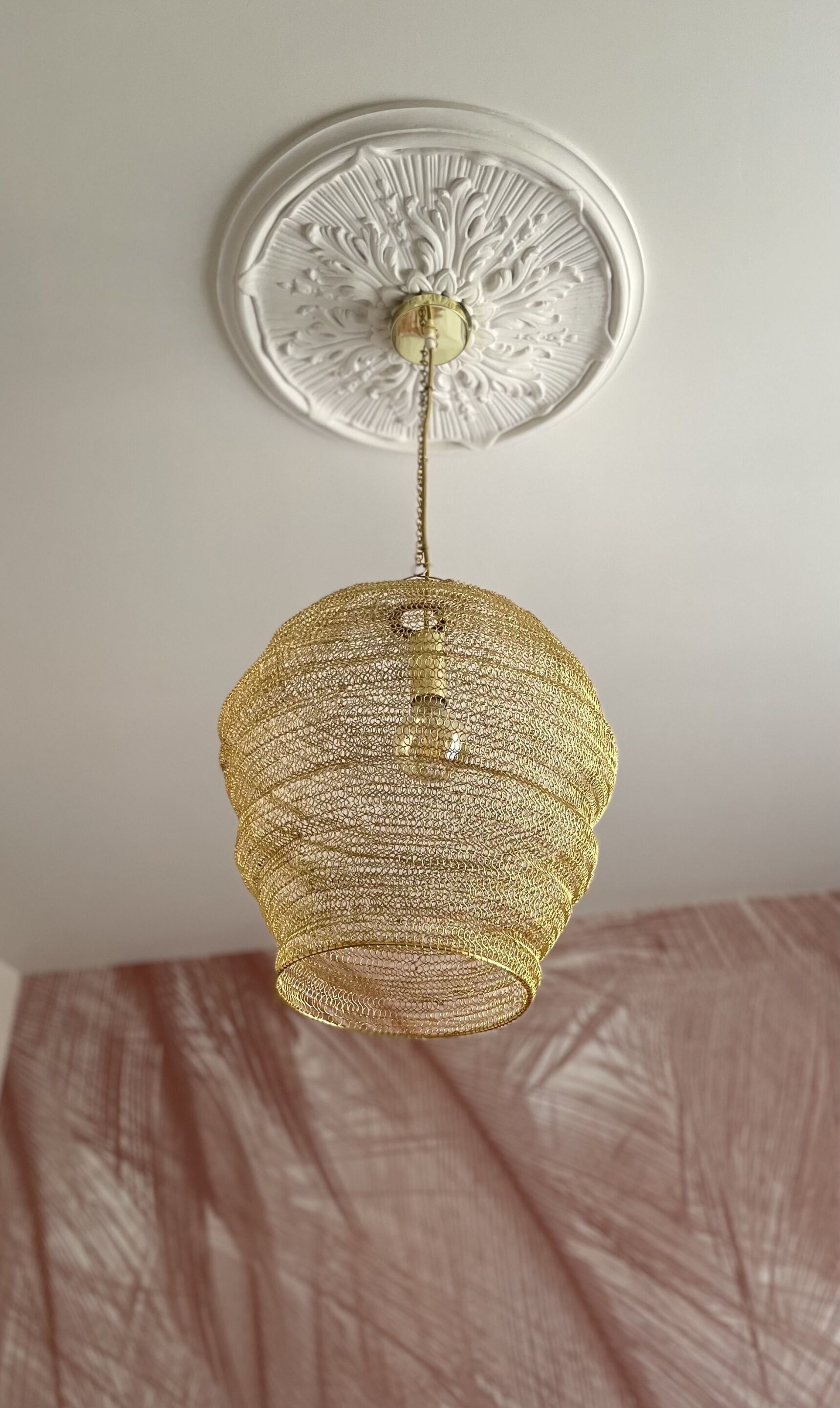 Een gouden hanglamp met een reliëfpatroon, bevestigd aan een wit plafond met een decoratieve centrale rozet.