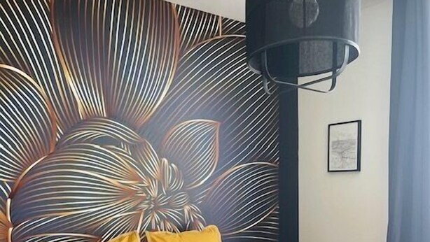 A bedroom with a bed, yellow and green pillows, a dark blue bedspread, and a wall with a leaf pattern. - Maison Le Beaulieu (Vichy)