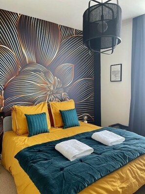 A bedroom with a bed, yellow and green pillows, a dark blue bedspread, and a wall with a leaf pattern. - Maison Le Beaulieu (Vichy)