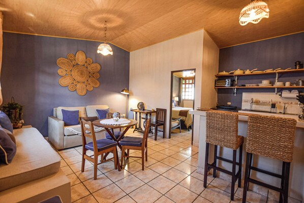 Una sala acogedora con sofá, sillas, una mesita y una cocina con estanterías y mostrador.