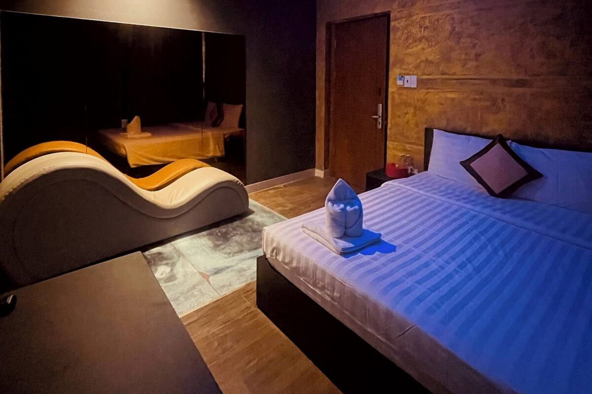 Ein modernes Hotelzimmer mit einem bogenförmigen Bett, Holzboden und einer Decke mit einer runden, blauen Leuchte.