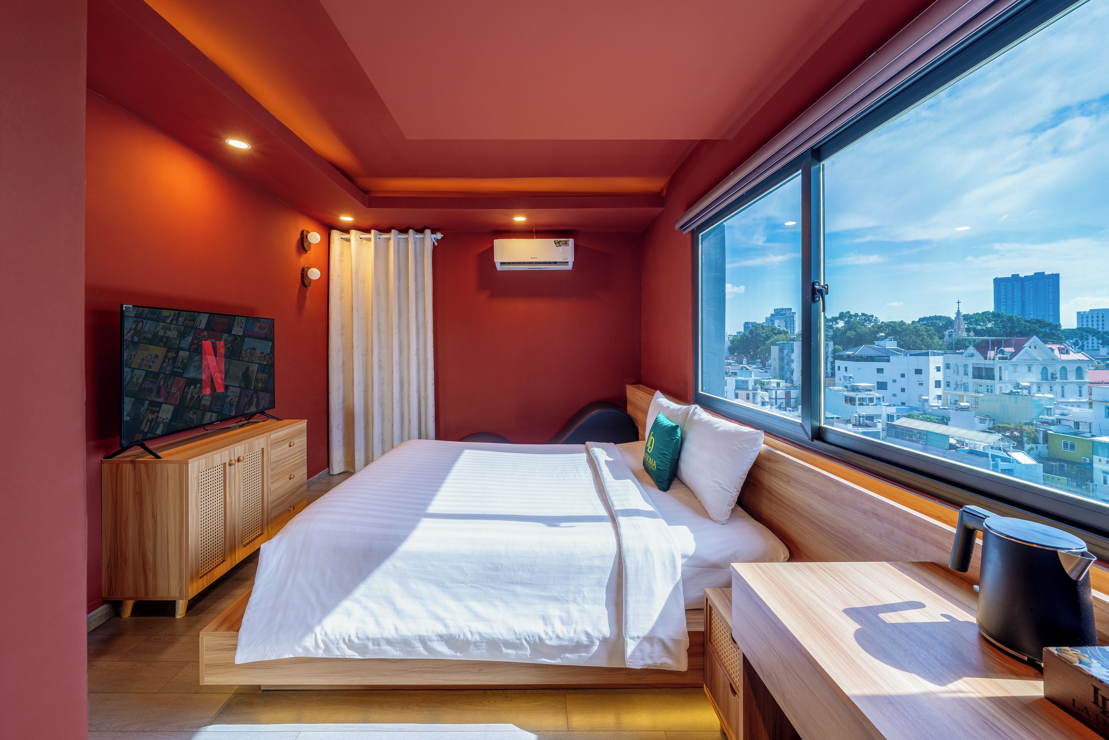Une chambre d’hôtel équipée d’un lit, d’une télévision, d’une fenêtre donnant sur la ville et d’un appareil de climatisation.