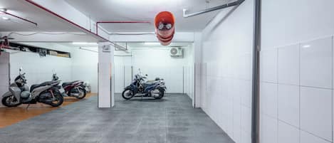 Un espacio interior limpio y bien iluminado, con paredes de baldosas y piso de concreto, que muestra dos scooters estacionados y grifería visible.