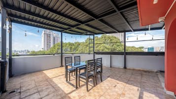 A covered outdoor seating area with a table and chairs, a view of a cityscape, and a tiled floor.