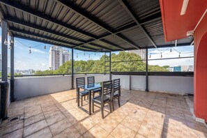 A covered outdoor seating area with a table and chairs, a view of a cityscape, and a tiled floor. - La Doma en Amour Hotel (Ho Chi Minh City)