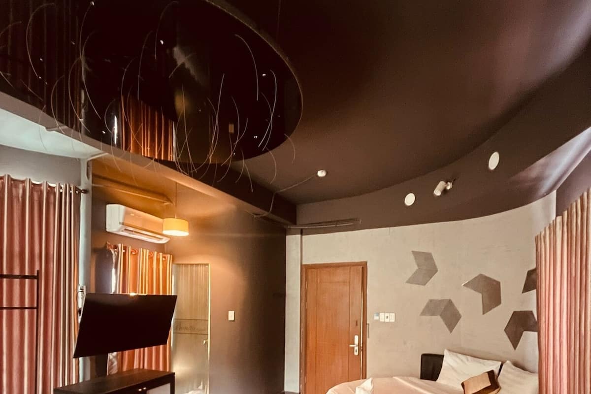 Ein modernes Hotelzimmer mit gewölbter Decke, einem Bett mit Kopfteil, einem Flachbildfernseher und einer kleinen Sitzecke mit Vorhängen.