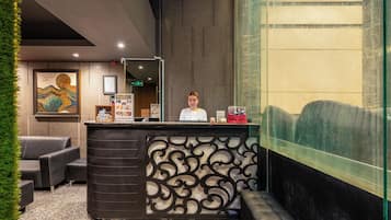A reception desk with a modern design, a framed artwork on the wall, and a seating area with a carpeted floor.