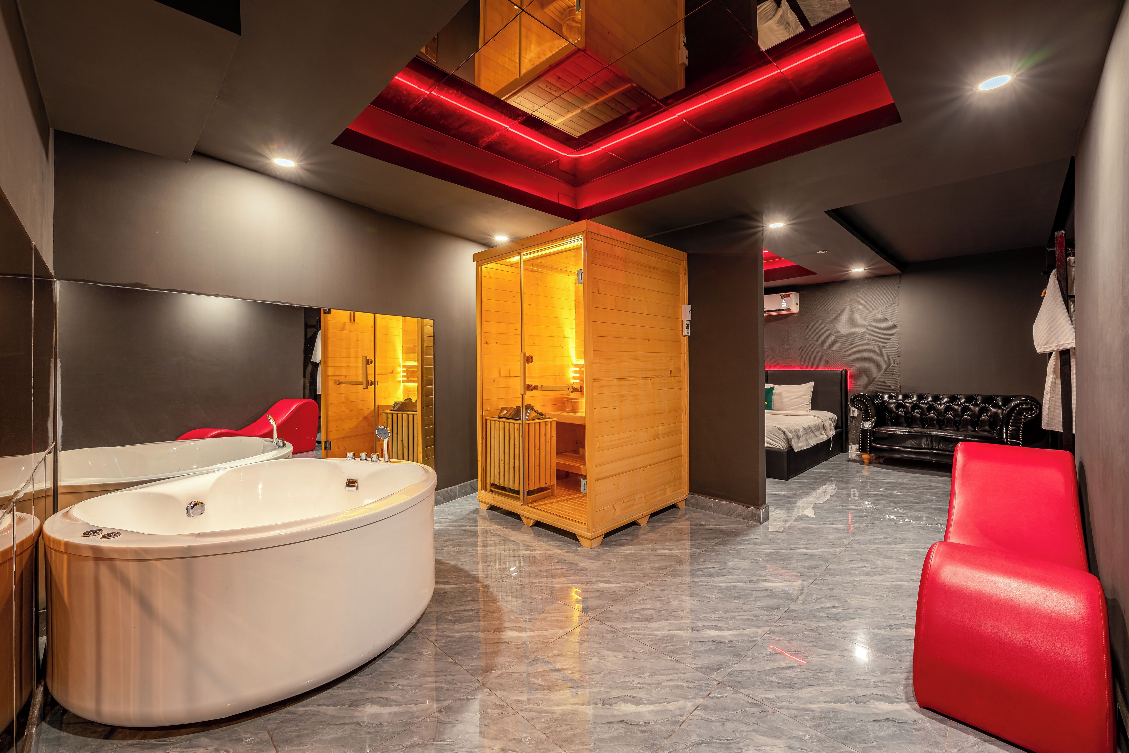 Une salle de bain moderne avec une grande baignoire, un sauna en bois et un fauteuil rouge.