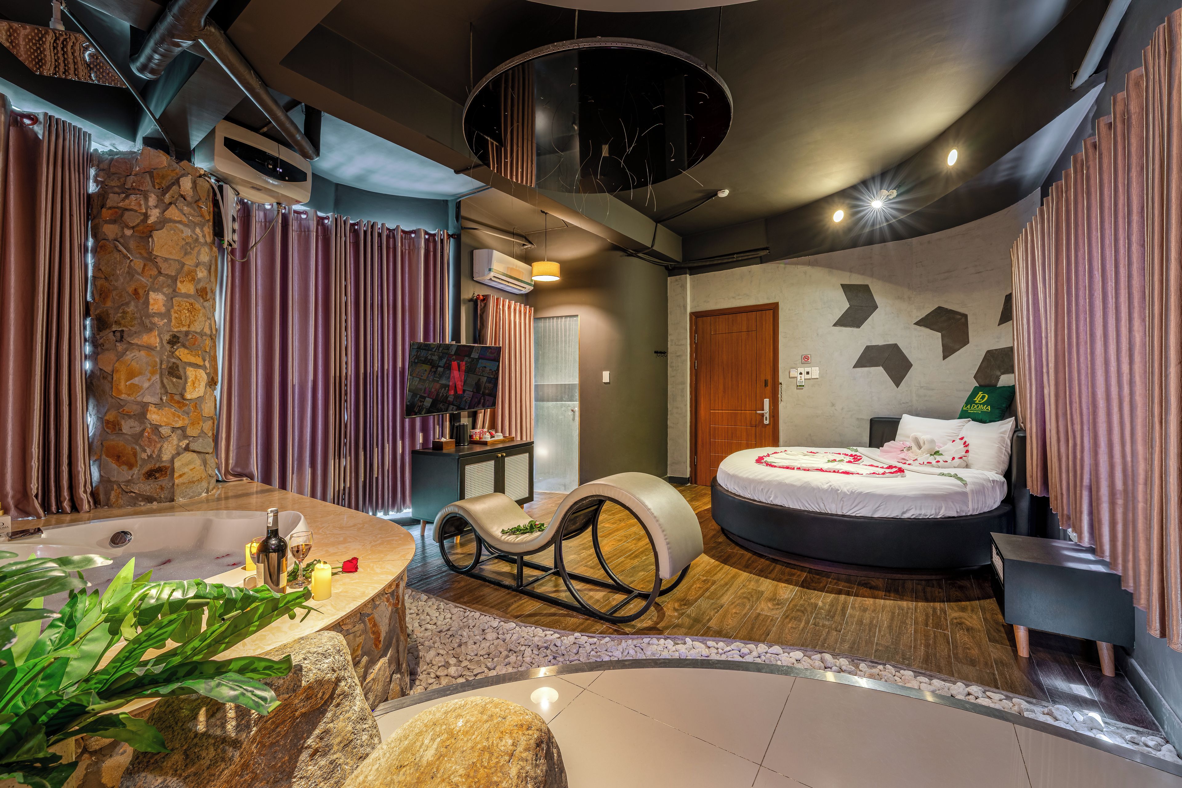 A modern bedroom with a stone wall, a round bed, and a bathtub.