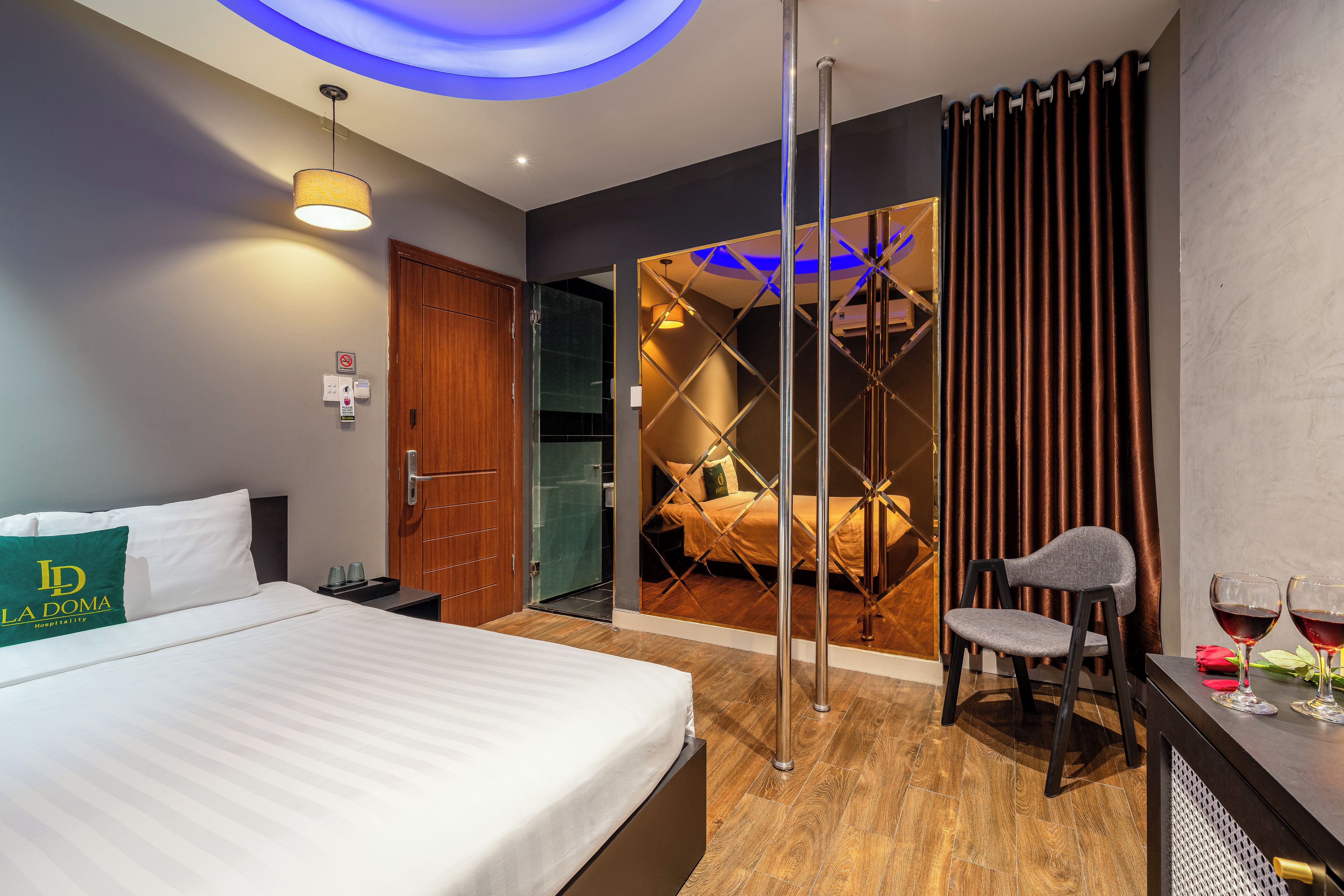 Ein Hotelzimmer mit einem Bett, einem Schreibtisch mit Stuhl, einer Glastrennwand und Blick auf ein weiteres Zimmer mit einem Bett.