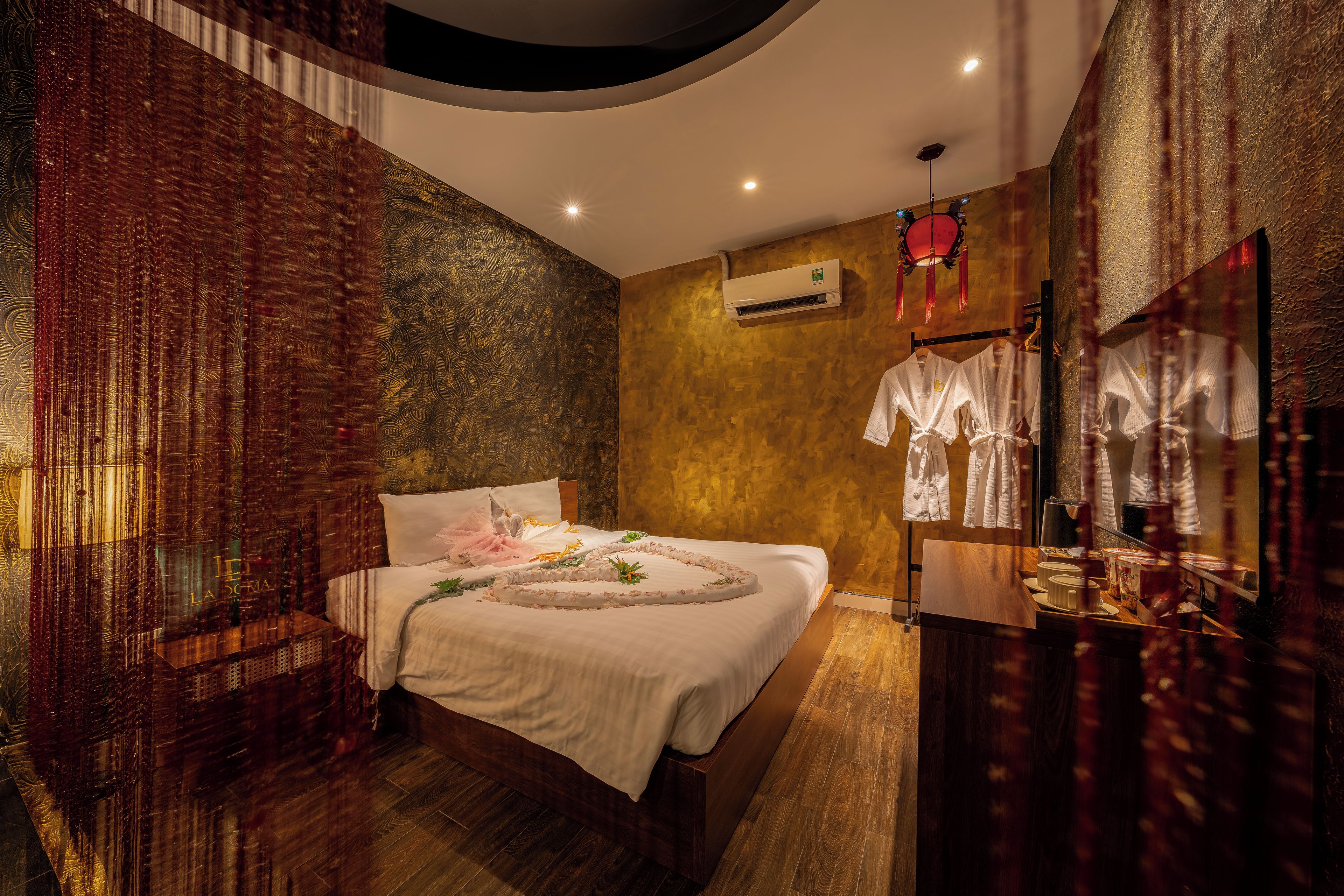 A bedroom with a bed, a wall-mounted air conditioner, and a mirror with hanging clothes.