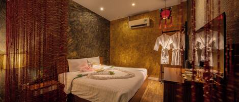 A bedroom with a bed, a wall-mounted air conditioner, and a mirror with hanging clothes.