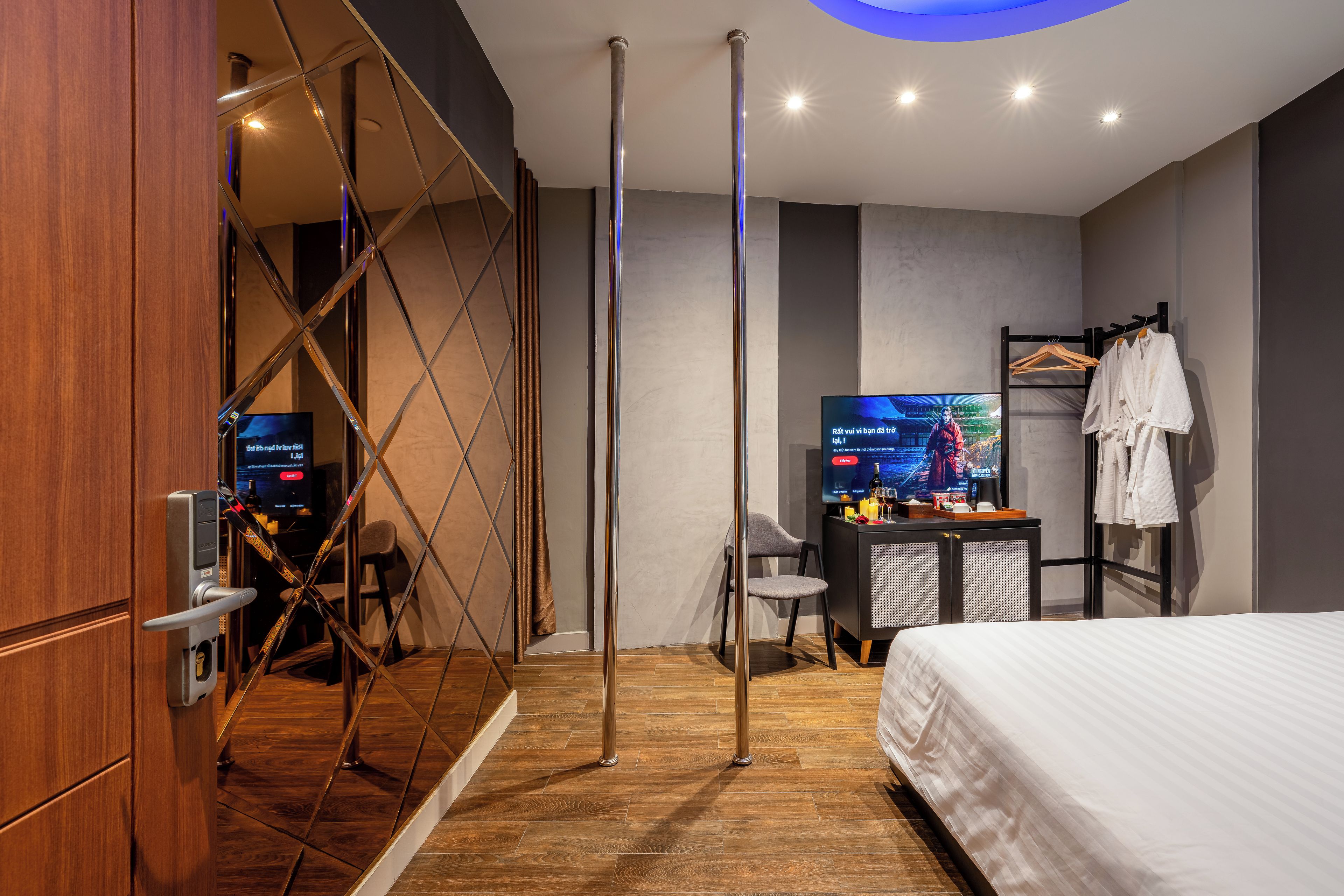 Ein modernes Hotelzimmer mit Bett, Schreibtisch mit Fernseher, Kleiderschrank und einem Badezimmer mit Glasabtrennung.