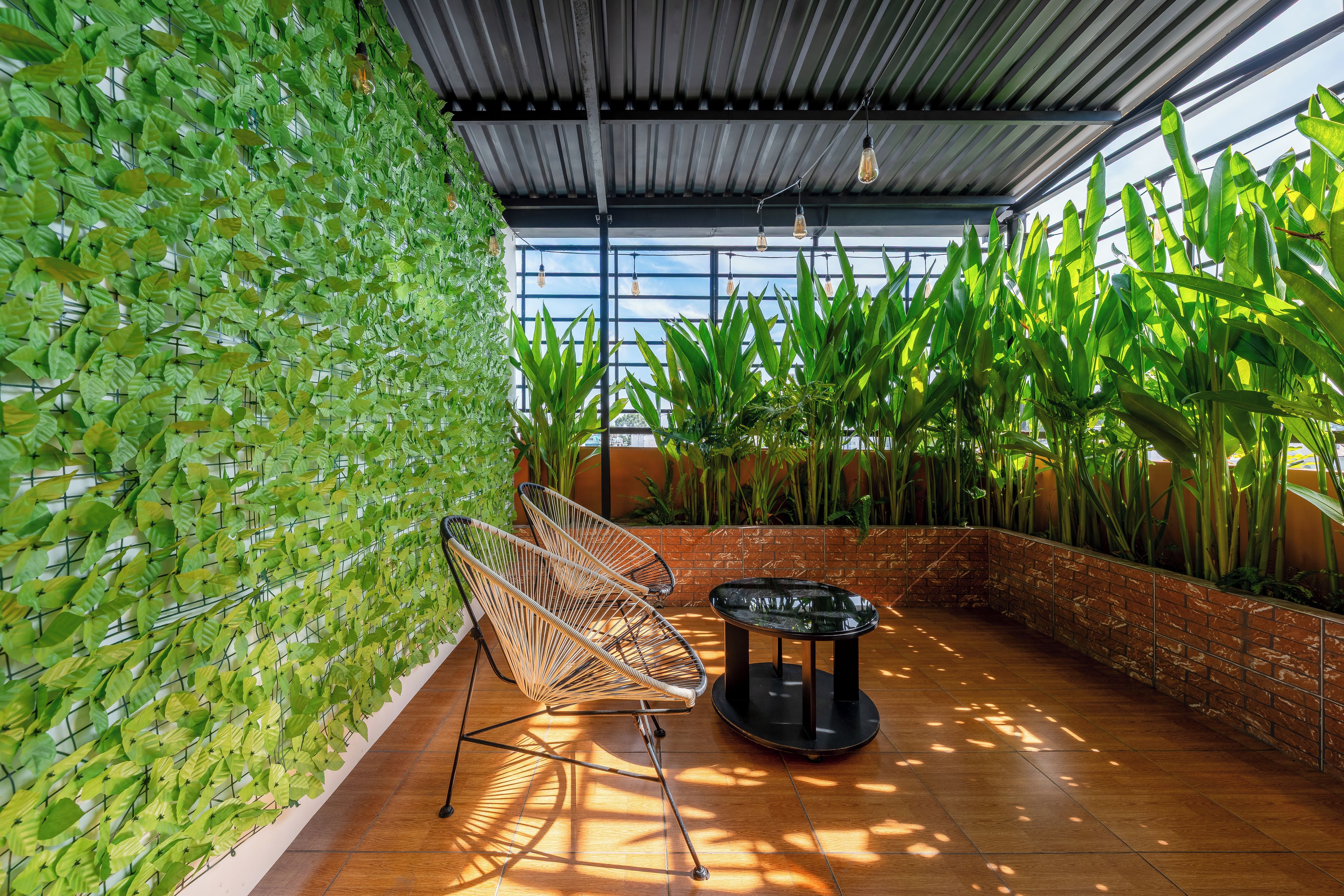 A room with a wall covered in green foliage, a seating area with a chair and a table, and tall plants against the wall.