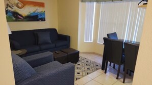 Ein Wohnzimmer mit einer Couch, Hocker und einem Essbereich mit Stühlen und Tisch.