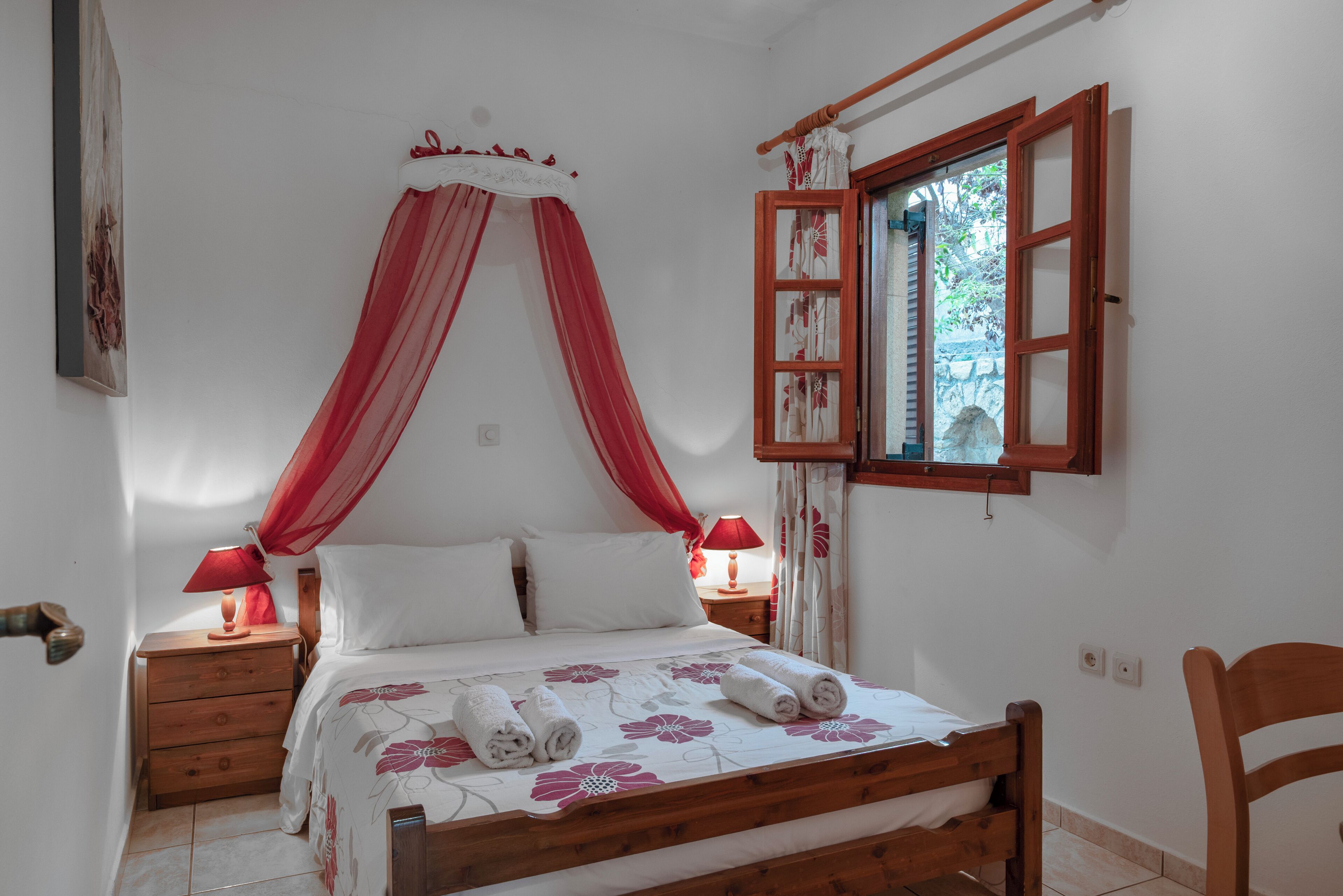 A bedroom with a wooden bed, red canopy, two bedside tables with lamps, and a window with curtains.