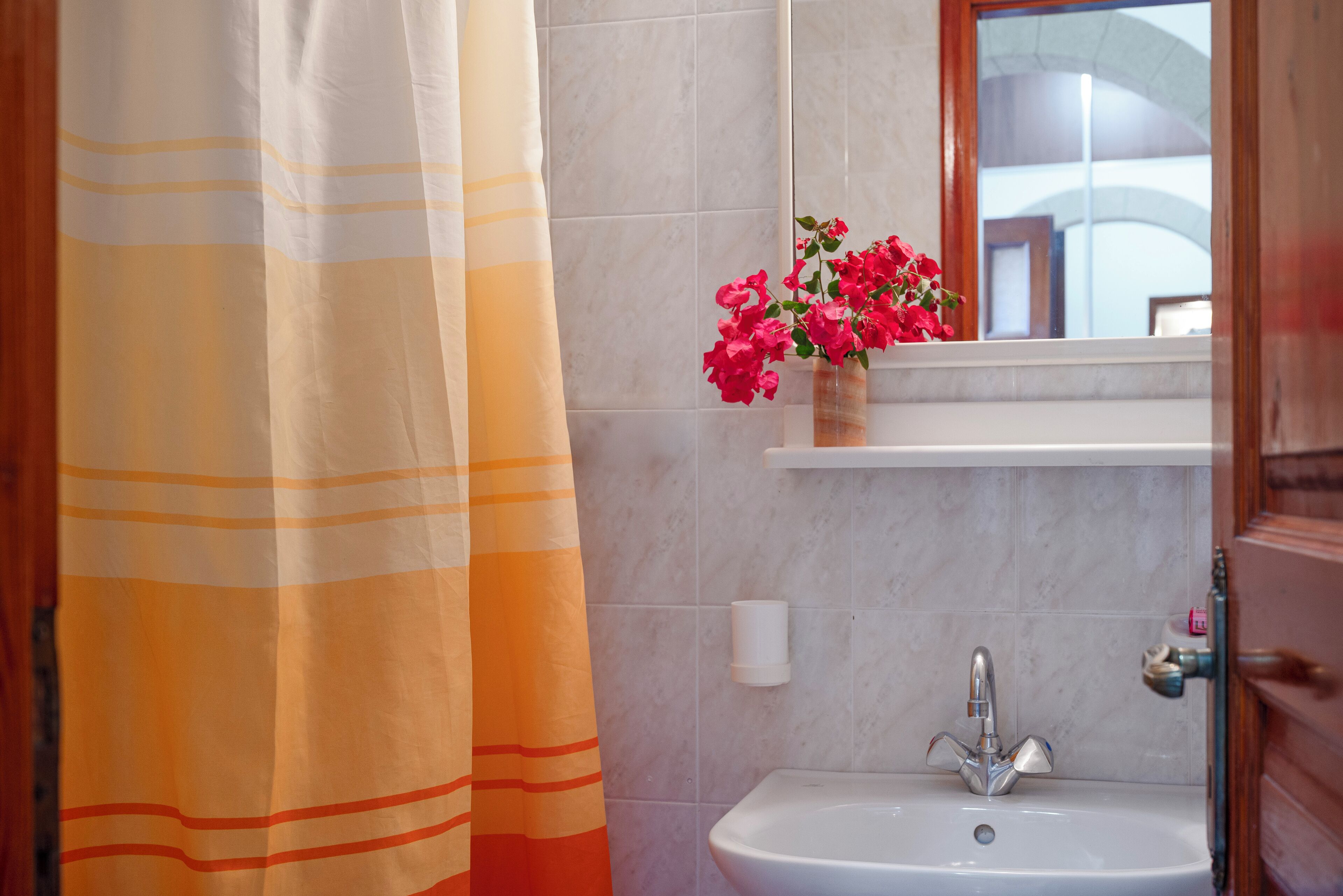 Une salle de bain avec un rideau de douche à rayures, un lavabo avec un miroir au-dessus et un vase rempli de fleurs posé sur le bord du lavabo.